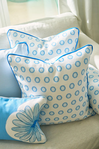 Three Calico Mini Floral Oversized Pillows adorn a light sofa: two display a blue mini floral pattern on white, and one features a bold blue flower. Each pillow is accented with bright blue piping for a decorative finish.
