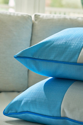 Two blue and gray decorative pillows, including the Spring Blue Blocks Oversized Pillow, are stacked on a light sofa, with natural sunlight highlighting the textured fabric for a calming, modern look.