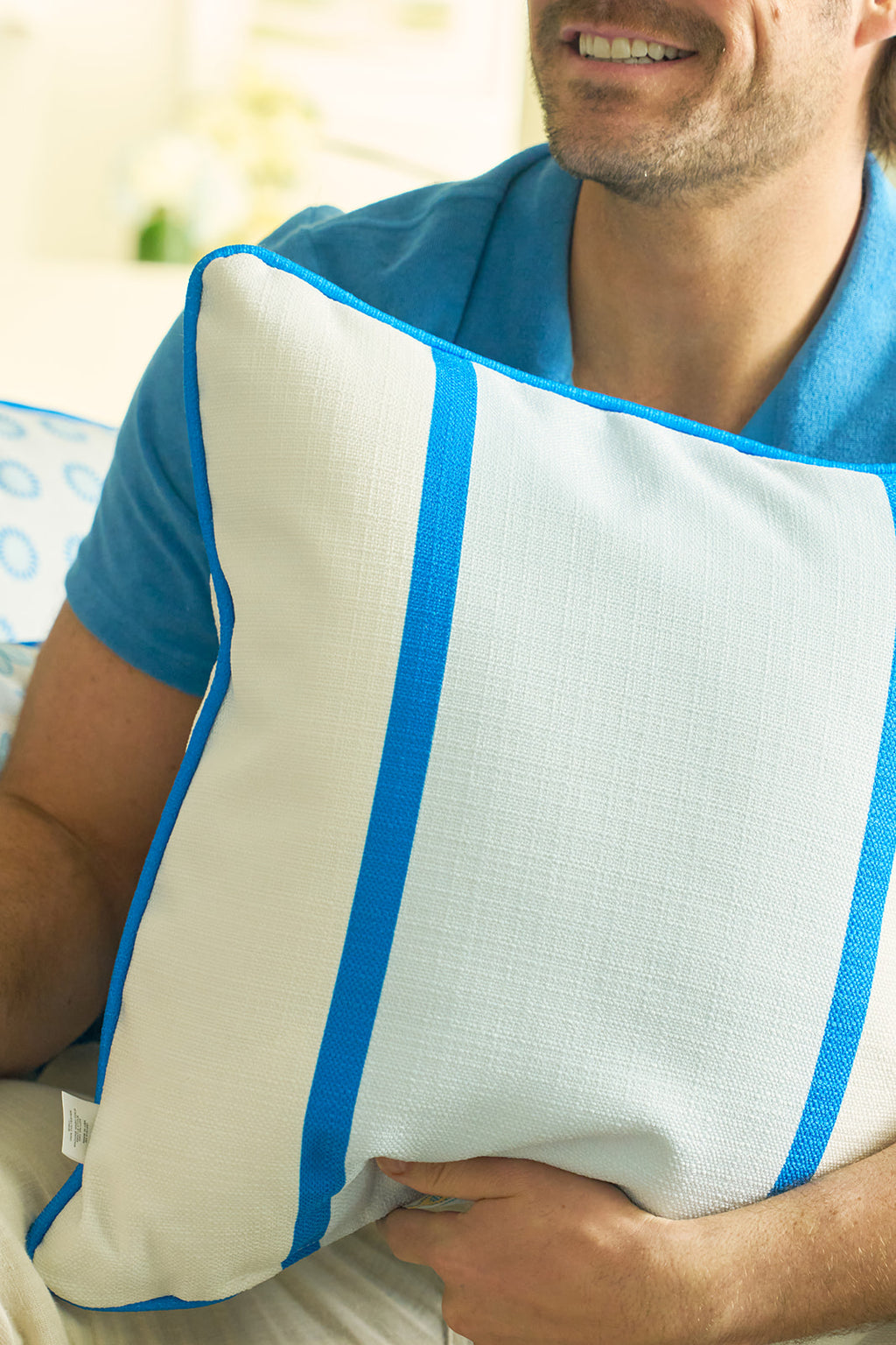 A man in a blue shirt smiles while holding the Line of Euro Blue Tiles Pillow, featuring a blue and yellow floral pattern inspired by Mediterranean villages and classic European elegance.