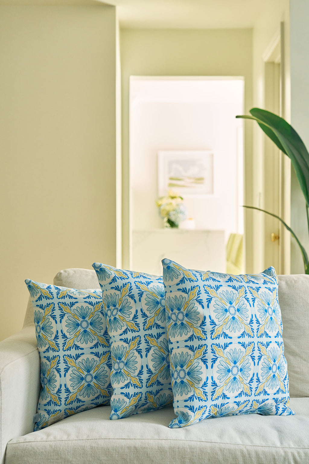 A man in a blue shirt hugs the Euro Blue Tiles Pillow, featuring a blue, yellow, and white floral design. Only the lower half of his smiling face is visible as the pillow adds charm to the scene.