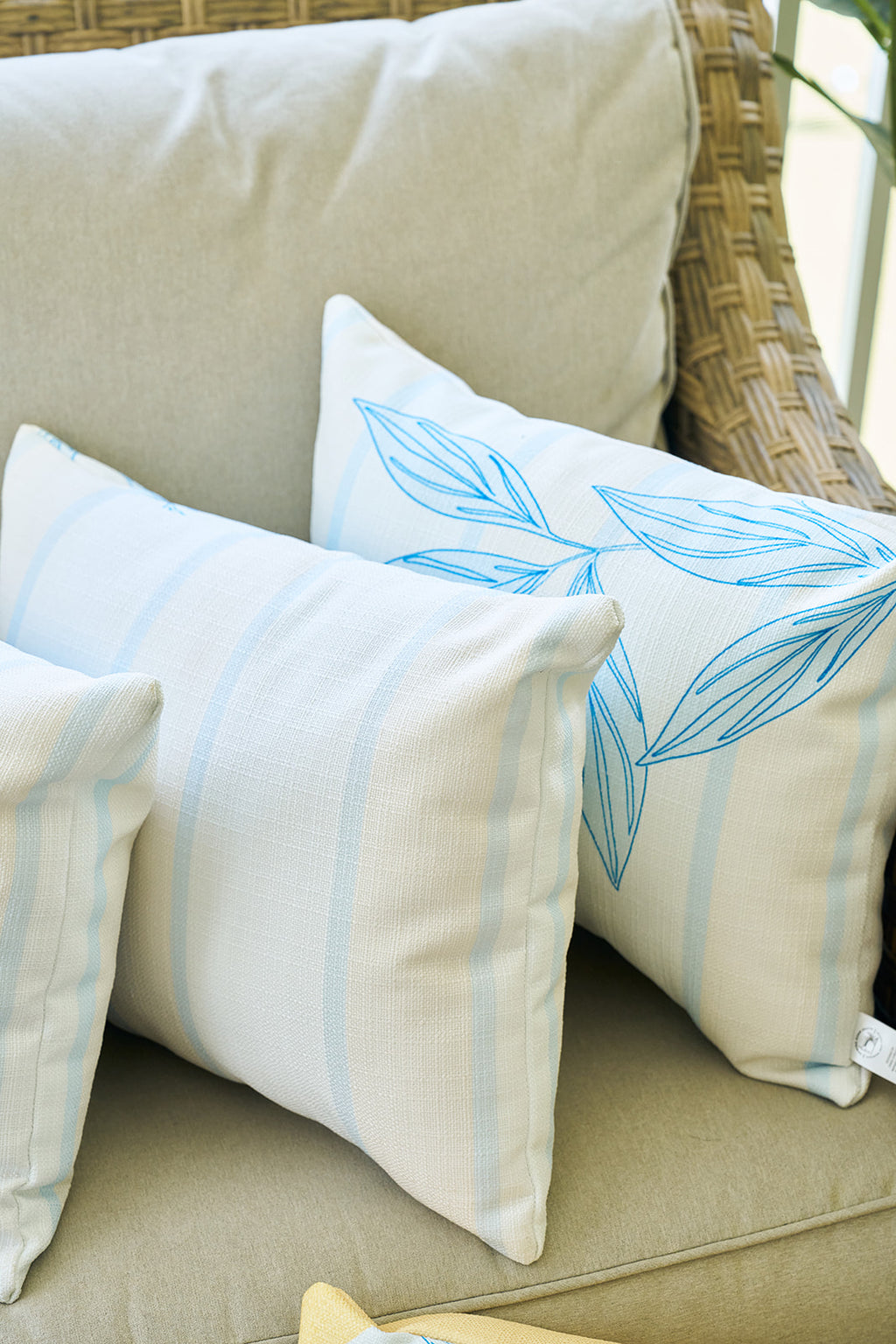 A man smiles while hugging the Lemons in a Line Lumbar Pillow, featuring blue leaf and yellow fruit designs. He wears a white shirt and beige pants, sitting in a bright setting with citrus-inspired decor.