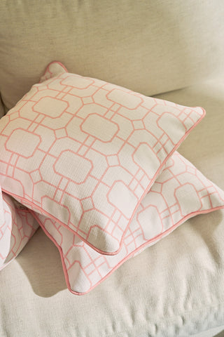 Two Pink Lattice Pillows with a blush hue, light pink geometric design, and pink piping rest neatly stacked on a beige sofa, creating a cozy and inviting look.