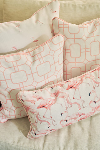 Four decorative throw pillows, including the Pink Lattice Pillow with a geometric lattice design and blush tones, showcase pink and white patterns and flamingo prints, all stylishly displayed on a beige fabric sofa.