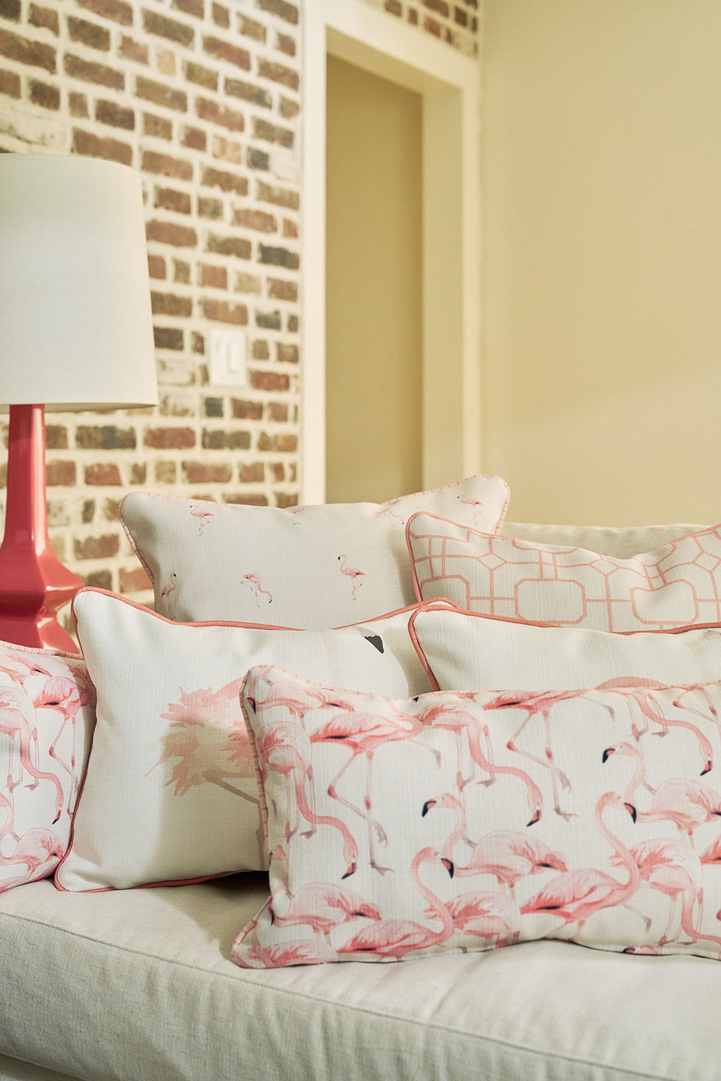 A smiling person in a light pink shirt holds the Flamingo Cluster Extended Lumbar Pillow, featuring the iconic Sewing Down South® pattern. White and pink geometric pillows in the background add to the coastal charm.