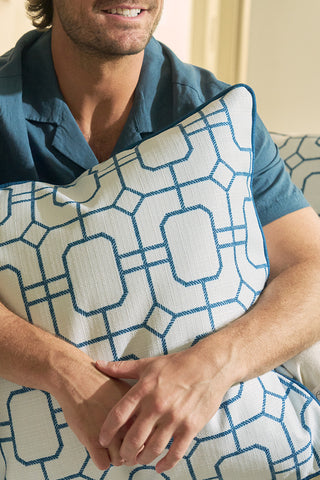 A man in a blue shirt, with only his mouth and arms visible, holds the Blue Lattice Oversized Pillow featuring a coastal blue geometric pattern while sitting in a brightly lit room.