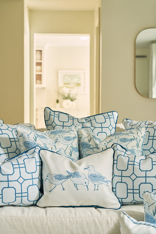 A cozy, softly lit living room features a light-colored sofa adorned with decorative throw pillows, including the Blue Lattice Oversized Pillow with geometric patterns and bird motifs.