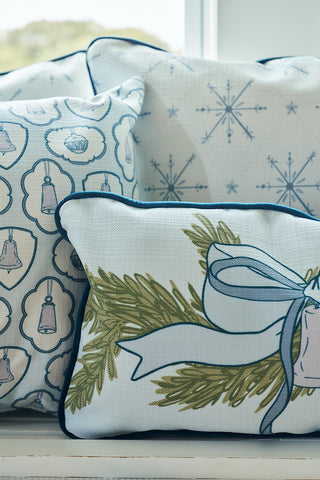 The Holiday Swag Extended Lumbar Pillow from Sewing Down South is arranged with other decorative pillows featuring snowflake designs and evergreen branches in front of a window.
