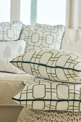 The Green Holiday Lattice Oversized Pillow is stacked with another decorative pillow on a beige pouf, while additional holiday-themed pillows decorate a cream-colored sofa in the background.