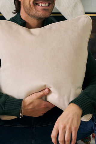 A smiling man in a dark green sweater sits holding the Nutcracker Stripe Pillow, in Angora, with his hands resting on the soft velvet pillow in front of his chest.