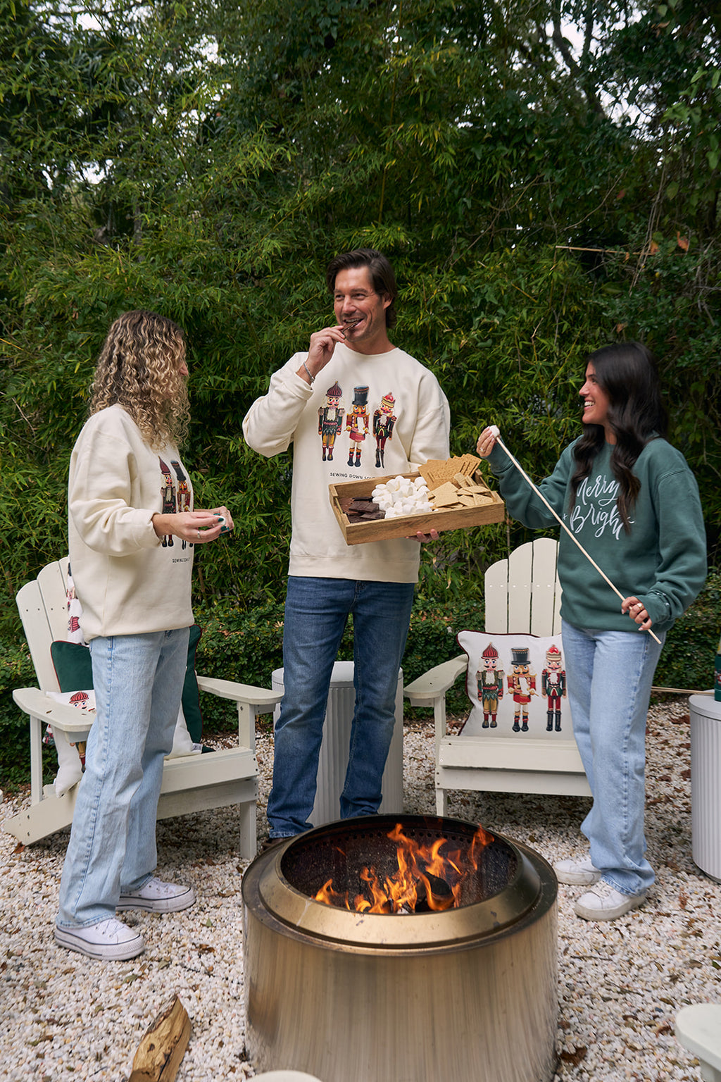 A smiling man wears the Nutcracker Crewneck, a cream festive sweatshirt featuring three colorful nutcrackers and SEWING DOWN SOUTH text. He stands outdoors with greenery in the background.