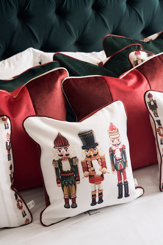 A cozy bed is adorned with a wine velvet pillow and Nutcracker Holiday Pillows featuring colorful soldiers, all set against a tufted dark green headboard for a festive look.