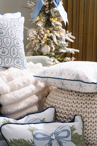 A cozy holiday scene with a decorated Christmas tree, the Luxe Snowflakes Oversized Pillow in blue with festive designs, a fluffy white blanket, and a knitted pouf, creating a warm and inviting atmosphere.