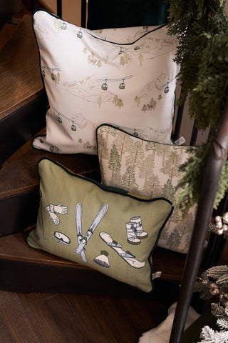 The Ski Resort Pillow, featuring ski lift and mountain motifs, sits among two other winter-themed pillows—one with a forest pattern and one with vintage ski decor—on wooden stairs.