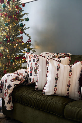 A decorated Christmas tree with red and green ornaments stands next to a green sofa featuring a Neutral Nutcrackers Pillow and a matching festive blanket draped over the side.