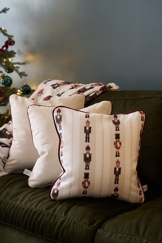 A green sofa with white pillows, including a Neutral Nutcrackers Pillow, sits beside a Christmas tree decorated with red and green ornaments and twinkling lights.