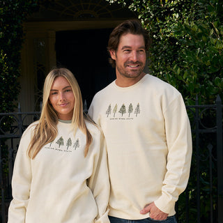 Two people wearing cream-colored sweatshirts with a tree design outdoors.