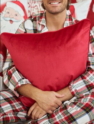A person in plaid pajamas holds a Vintage Repeating Santa Pillow, with festive décor and Santa-themed details in the background. Only the lower part of their smiling face is visible.