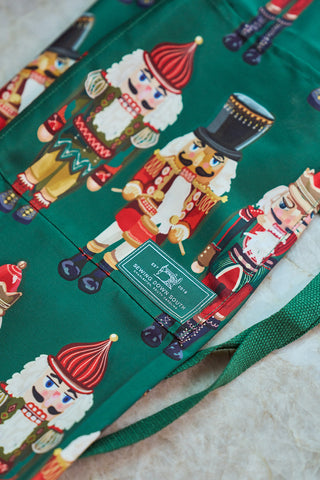 The Nutcracker Apron is green with colorful nutcracker soldier designs, an adjustable neck strap, and a sewn-on Sewing Down South label on a light background.
