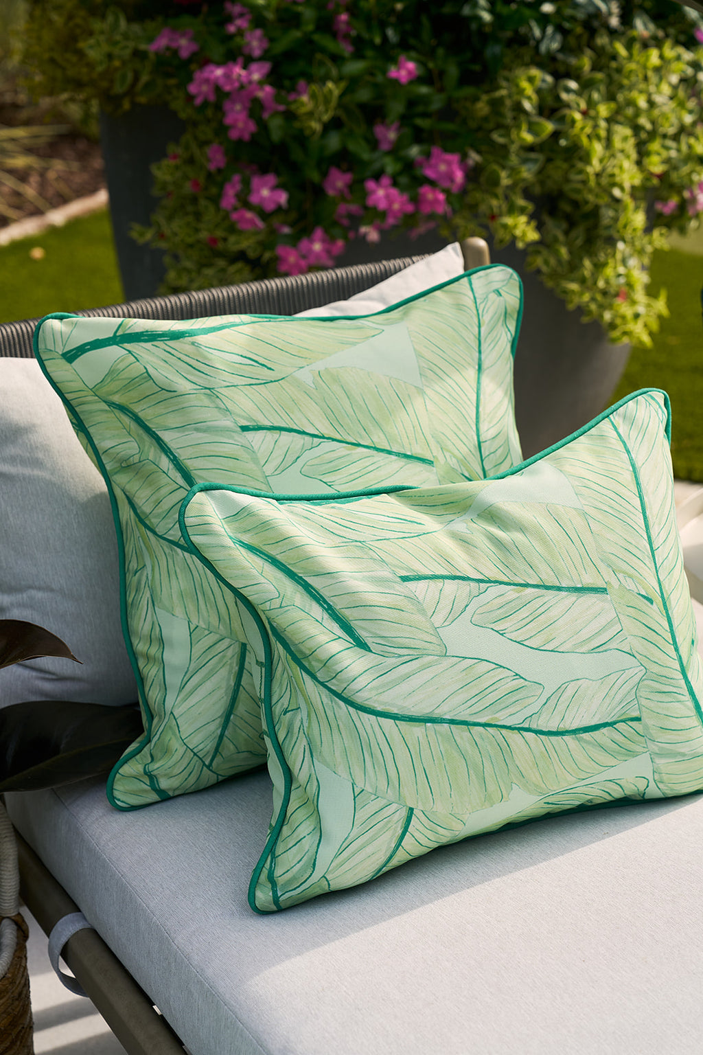 A person in a floral shirt holds the vibrant Banana Leaves Outdoor Pillow, with the Sewing Down South® pattern, while smiling slightly against a blurred green backdrop.