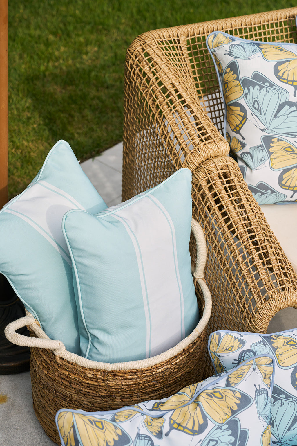 A person in a yellow shirt holds a Butterfly Stripe Lumbar Outdoor Pillow with a delicate yellow butterfly illustration. The persons face is partially visible as they sit outdoors, enjoying the day with their cozy accessory.
