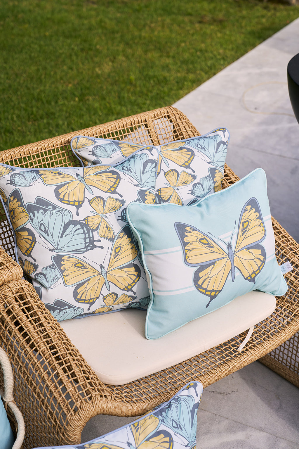 A person in a yellow shirt holds the Sewing Down South® Butterfly Scatter Outdoor Pillow, featuring vibrant blue and yellow butterflies. Their smile and arms are visible against a blurred background, highlighting the pillows charm.