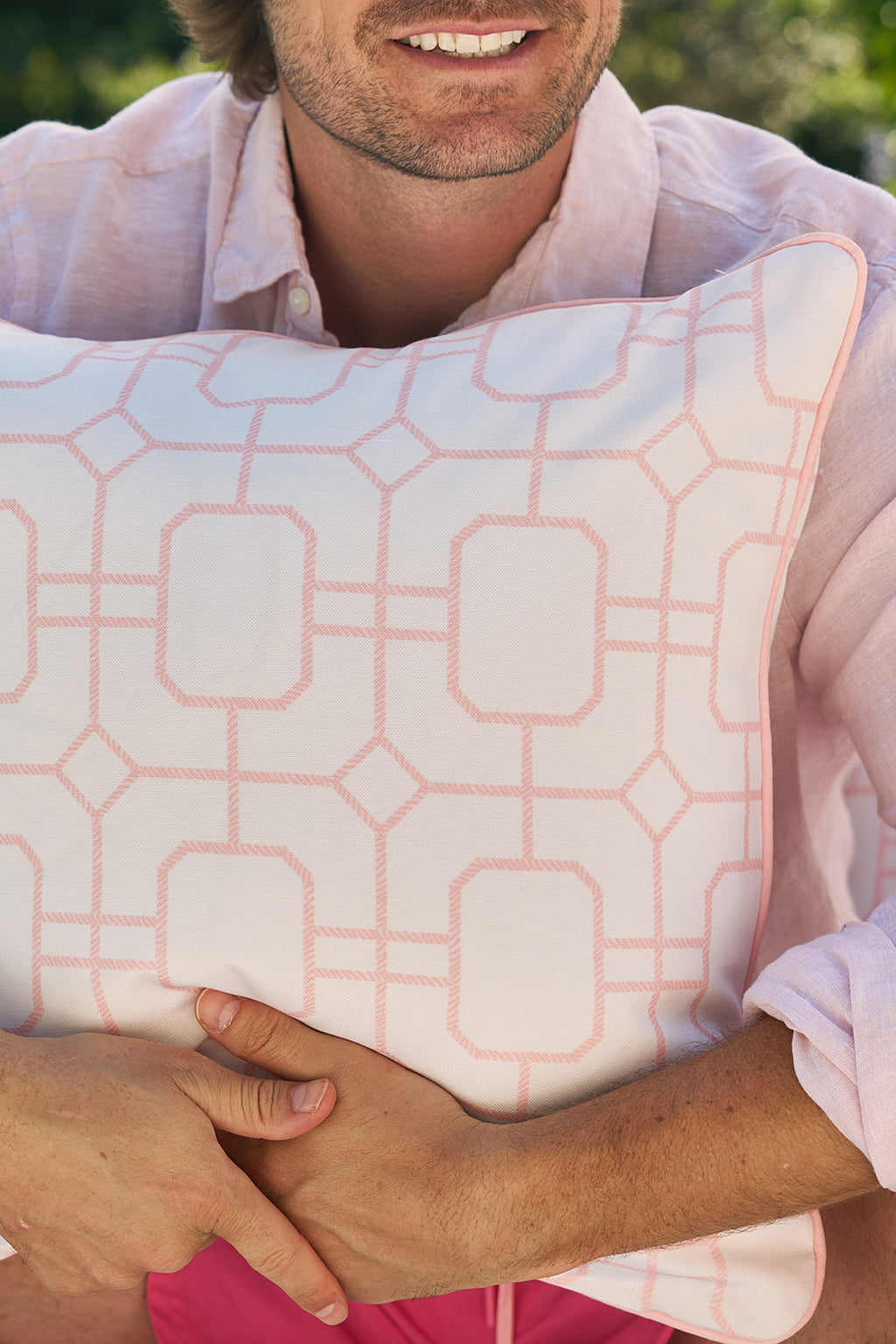 Four Pink Lattice Outdoor Pillows crafted with SDS Shield® Outdoor Fabric adorn a light sofa by the aqua pool, enhancing charm and durability. A wooden umbrella pole complements the serene setting.