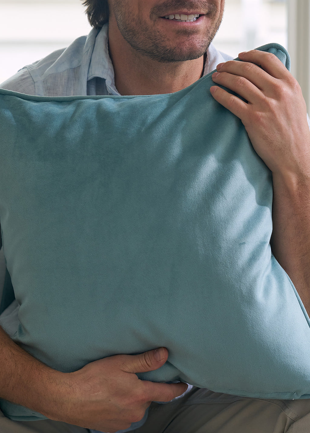 A person in a light blue shirt sits holding a Victorian Floral Stripe Pillow from the Sewing Down South® Bee & Florals Collection. The pillow features light blue and green floral embroidery on a white stripe with solid blue borders, with the persons face partially visible.
