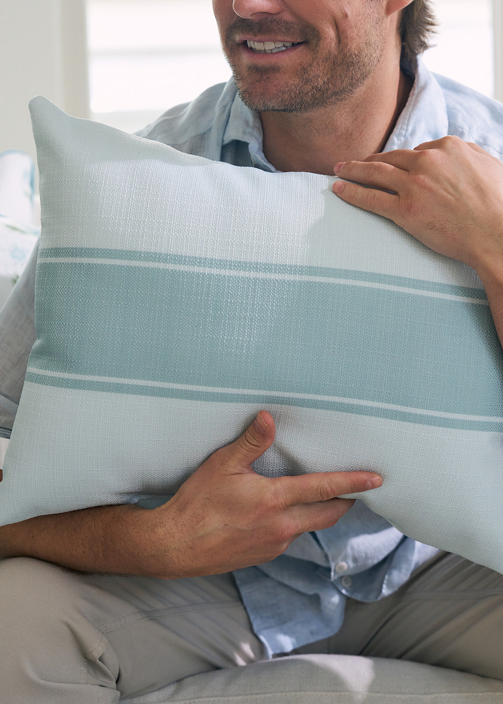 A person wearing a light blue shirt and beige pants, embodying Sewing Down South® style, holds the Bee & Florals Collection: Victorian Floral Stripe Lumbar Pillow. Proudly made in the USA, it features a light blue floral design with embroidered flowers in soft green and white.