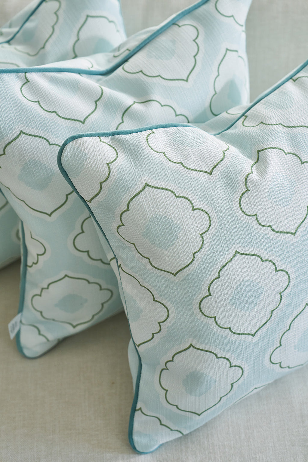 A man in a light blue shirt is arranging a Bee & Florals Collection: Victorian Tile Pillow and other patterned blue and white pillows on a sofa. The naturally bright room, filled with sunlight through the window, creates an inviting scene reminiscent of Sewing Down Souths style.