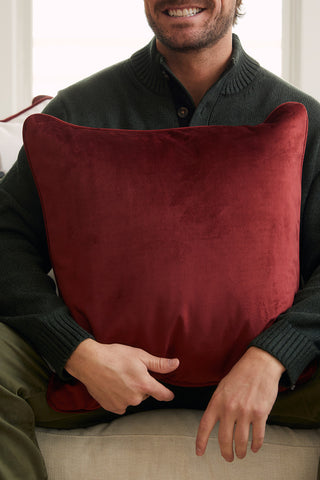 A person in a dark sweater sits on a couch, smiling and holding the Nutcracker Holiday Pillow on their lap, adding festive charm to the scene.