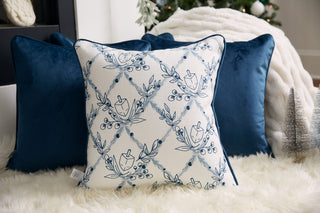 The Floral Hanukkah Pillow, featuring blue floral and geometric designs, is displayed in front of two navy pillows on a white rug with a Christmas tree and festive decor in the background.