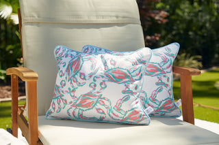 A beige outdoor chair with SDS Shield® Outdoor Fabric and wooden armrests sits in a garden setting, showcasing a vibrant Coral Crab Craze Lumbar Outdoor Pillow.