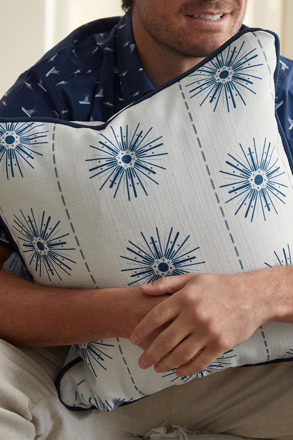Two Navy Starburst Pillows from the Coastal Collection, featuring dark piping, rest on a knitted surface. More pillows from Sewing Down South can be seen in the background on a cream sofa next to a partially visible potted plant.