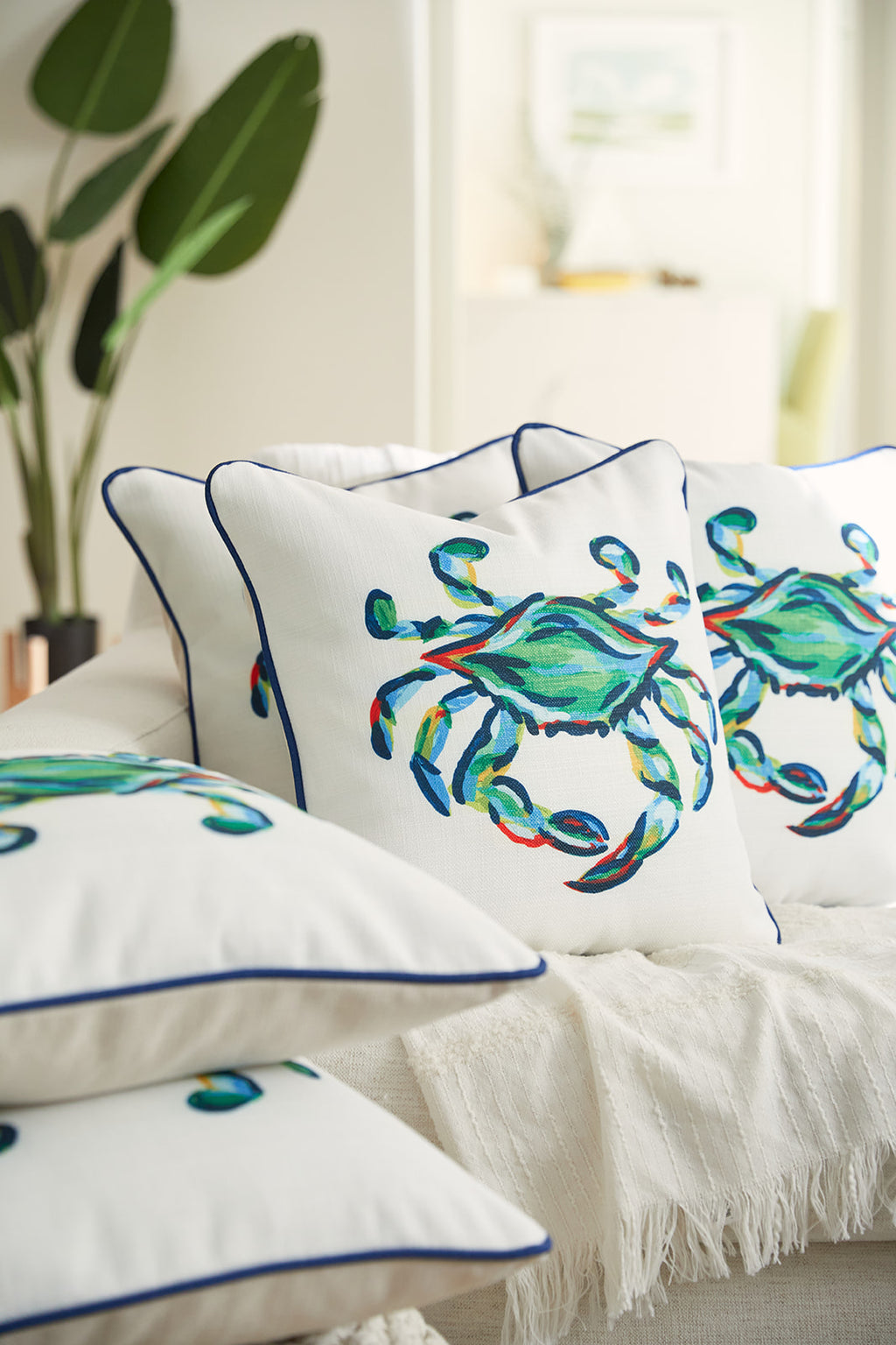 A man relaxes on a couch, clutching The King Crab Pillow with Navy. His blue shirt, featuring small boat patterns, complements the vibrant design of this Sewing Down South item. A lush green plant adds a touch of nature to the scene.