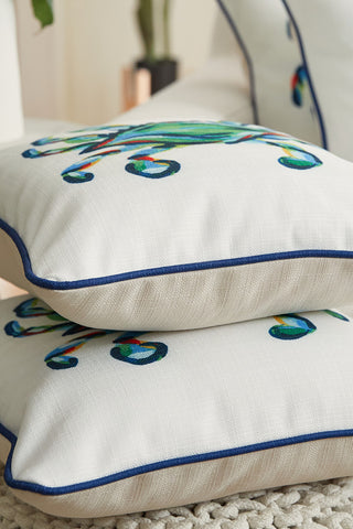 Two decorative pillows from the Coastal Collection feature white covers with colorful, abstract embroidery. The King Crab Pillow with Navy boasts blue piping around the edges and is set on a textured, light-colored surface.
