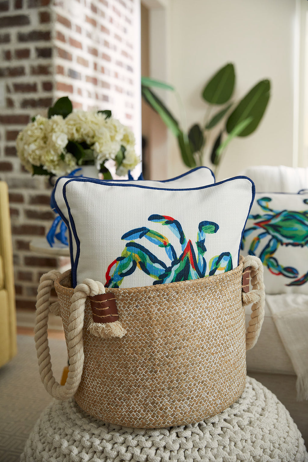 A person in a blue patterned shirt holds The King Crab Lumbar Pillow with Navy from the Coastal Collection, displaying vibrant hues of green, blue, and red. The image captures their relaxed demeanor, though they are partially cropped out.