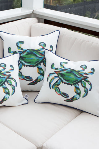 Three Outdoor King Crab Lumbar Pillows with navy accents, crafted from SDS Shield® Outdoor Fabric, adorn a beige sofa on a patio. The setting is completed by a black fence backdrop, creating a coastal-themed ambiance.