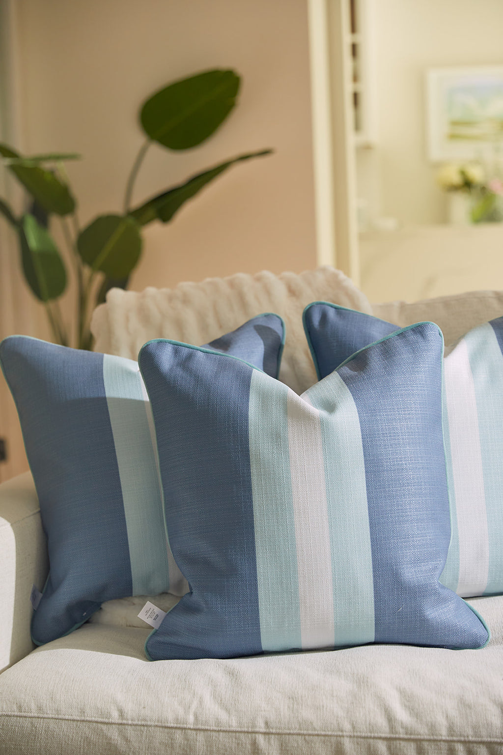 A man with short hair and a beard relaxes on a couch, resting his head on a Bee & Florals Collection: Bee Stripe Pillow from Sewing Down South. In a light blue shirt, he gazes thoughtfully into the distance.