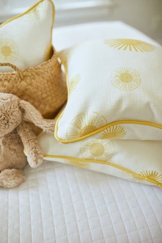 The Kids Collection: Sun Pillow features two white pillows with yellow floral patterns resting on a white quilted mattress. A plush bunny and woven basket nearby add to the cozy, inviting scene typical of Sewing Down Souths charming designs.