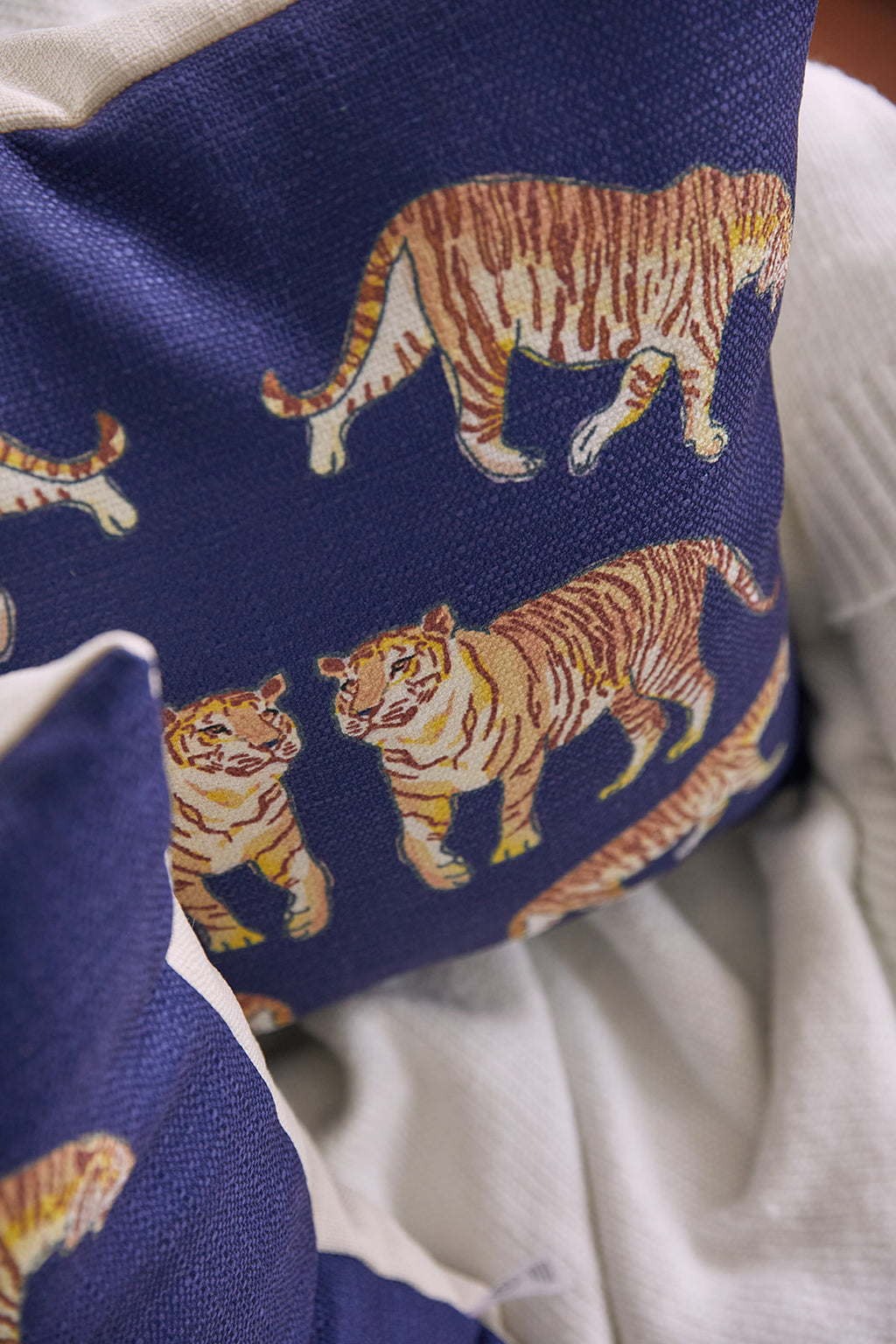 A person in a dark shirt holds the On The Prowl Midnight Pillow, decorated with tiger illustrations for an exotic touch. They sit against a softly lit backdrop, highlighting the animal pattern.