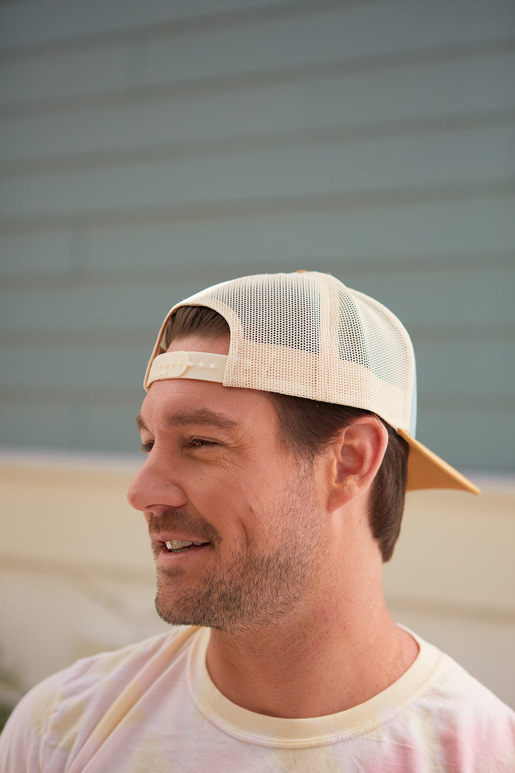A man in a Sewing Down South Leather Patch Trucker in Smoke Blue smiles, touching the brim, with a softly blurred background highlighting his relaxed demeanor.