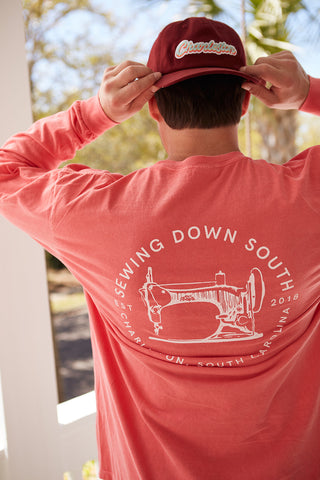 Adjusting their vintage-style red hat, theyre outdoors in sunlight wearing a Sewing Down South Long-Sleeve Logo Tee in a coral hue. Made from 100% ring-spun cotton, the tee features a white sewing machine logo and Sewing Down South, Charleston, South Carolina, 2018 text.