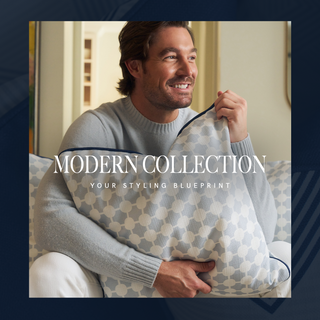 A smiling man in a light gray sweater sits on a couch, holding a decorative pillow with a geometric pattern. Text overlay reads: “Modern Collection. Your Styling Blueprint.”.