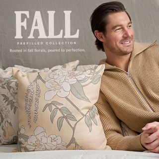 A man in a tan zip sweater sits on a sofa with beige floral pillows. Text reads: FALL PREFILLED COLLECTION - Rooted in fall florals, peared to perfection.