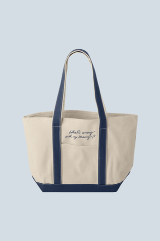 The WWWMS Embroidered Script Canvas Tote is a heavyweight cotton bag with navy blue handles and trim, featuring "Whats wrong with my sewing?" in handwritten script. A Bravocon exclusive, it's shown against a light blue background.