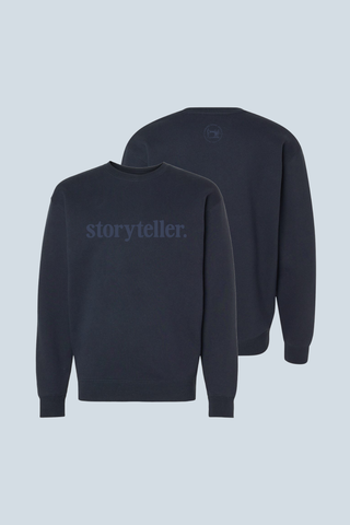 Two navy blue Storyteller Embroidered Crewneck Sweatshirts shown front and back; “storyteller.” appears in large, subtle text on the front, with a small circular logo near the back neckline—a Bravocon exclusive.
