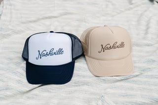 Two SDS Nashville Rope Trucker Hats are on a textured surface; the left hat is white with black mesh and brim, while the right is beige. Both feature Nashville embroidery and have an adjustable snapback for a perfect fit.