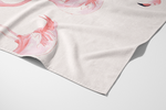 A close-up of the Flamingo Beach Towel, made from soft cotton and showcasing a watercolor pink flamingo design, is shown neatly folded with part of the illustration visible.