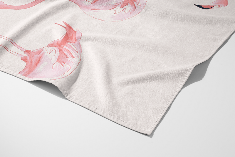 A close-up of the Flamingo Beach Towel, made from soft cotton and showcasing a watercolor pink flamingo design, is shown neatly folded with part of the illustration visible.