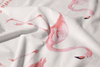 The Flamingo Beach Towel is made of white cotton and features a printed pattern of pink flamingos in various poses. Slightly wrinkled fabric adds soft shadows and texture to this exclusive design.